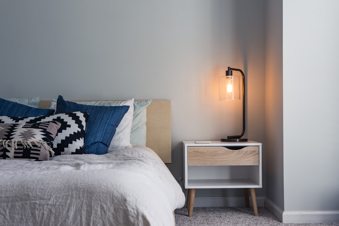 Rumpled white linen and a wooden bedside table in warm lamp light