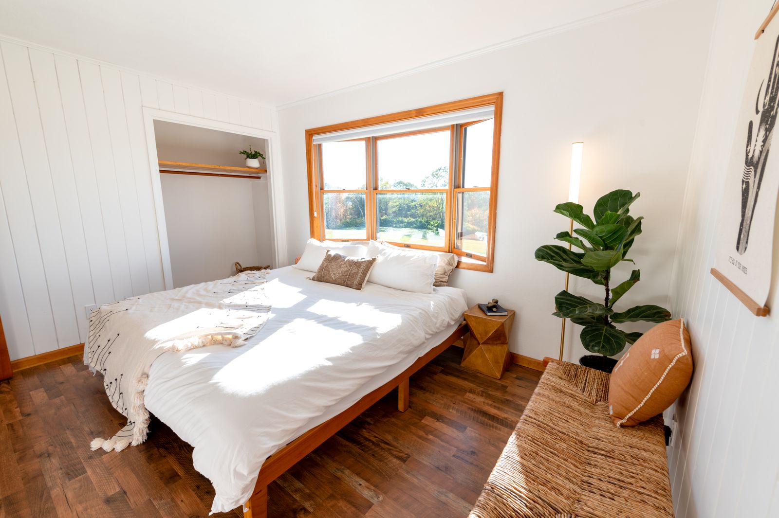 White linen bedding on a wooden bed beside a garden window