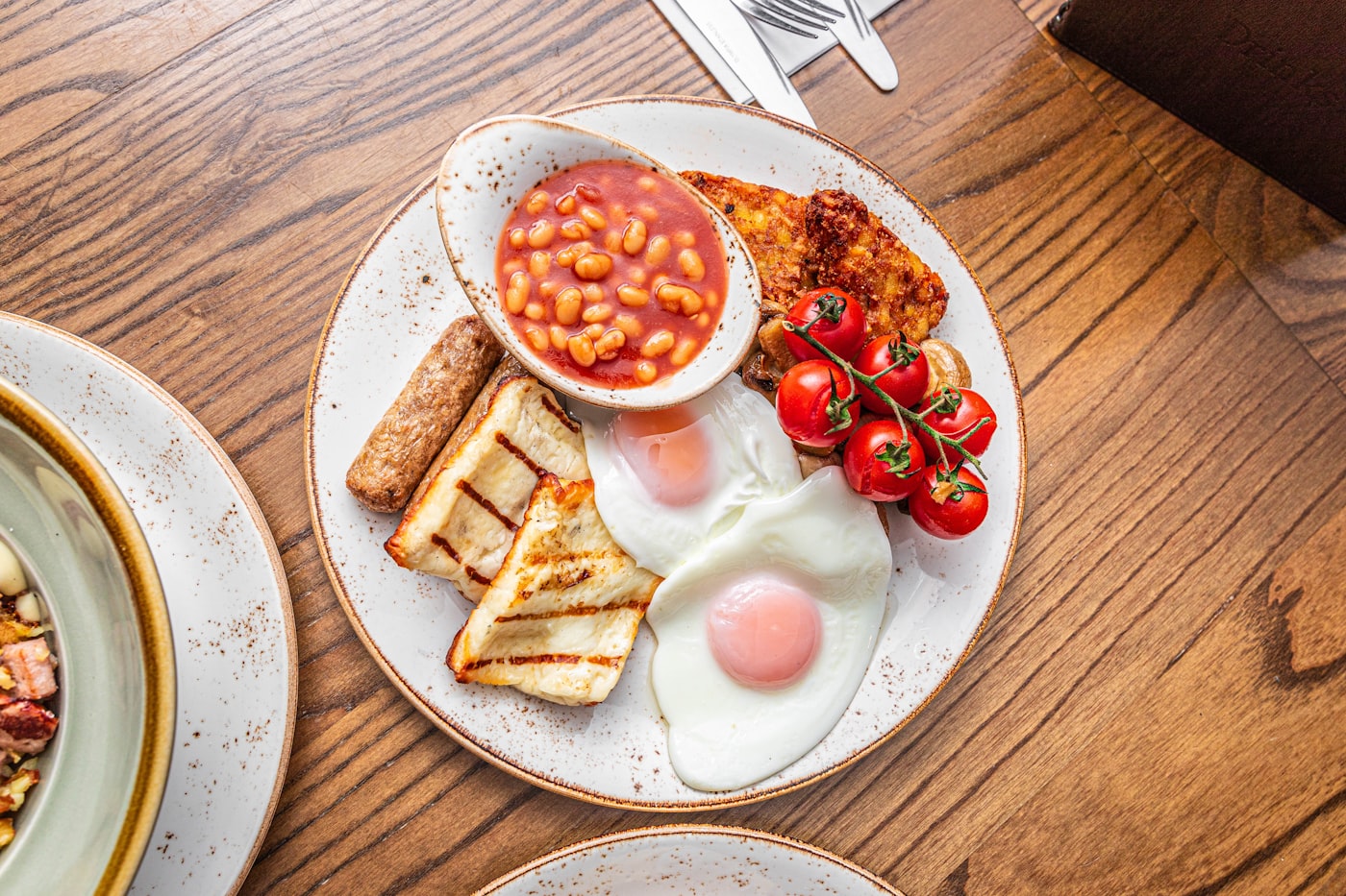 A cooked breakfast of eggs, tomatoes, mushrooms and beans on a wooden table