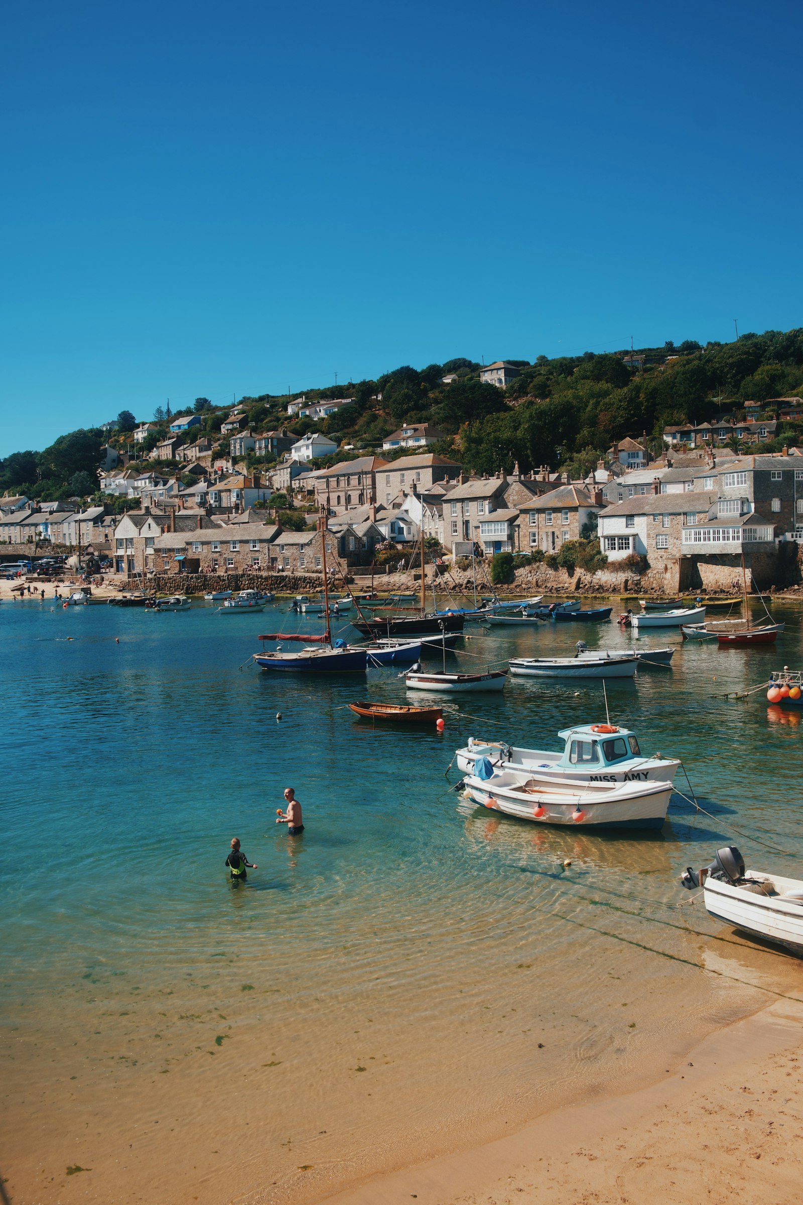 Small boats on clear water below a hillside of stone cottages